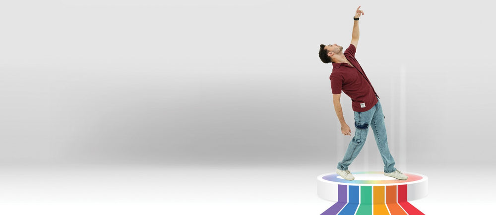 Person standing on a platform with a rainbow pattern, reaching towards a white wall.