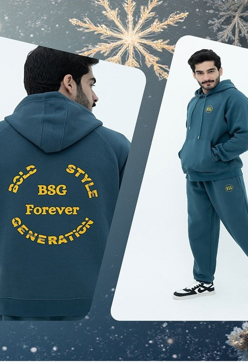 Man wearing a teal hoodie and pants with text, standing against a snowy background.