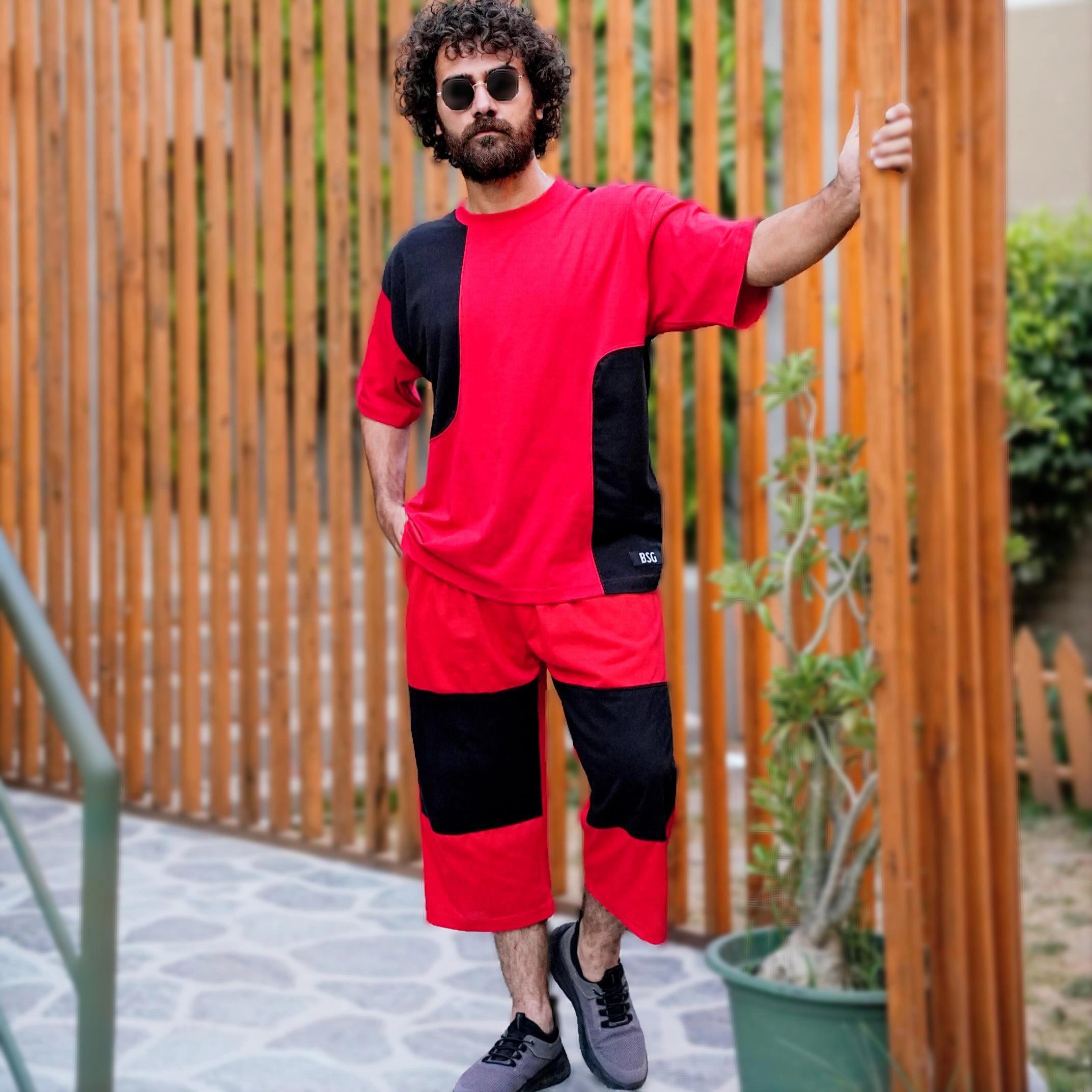 Man wearing a red and black outfit standing outdoors near a wooden fence.