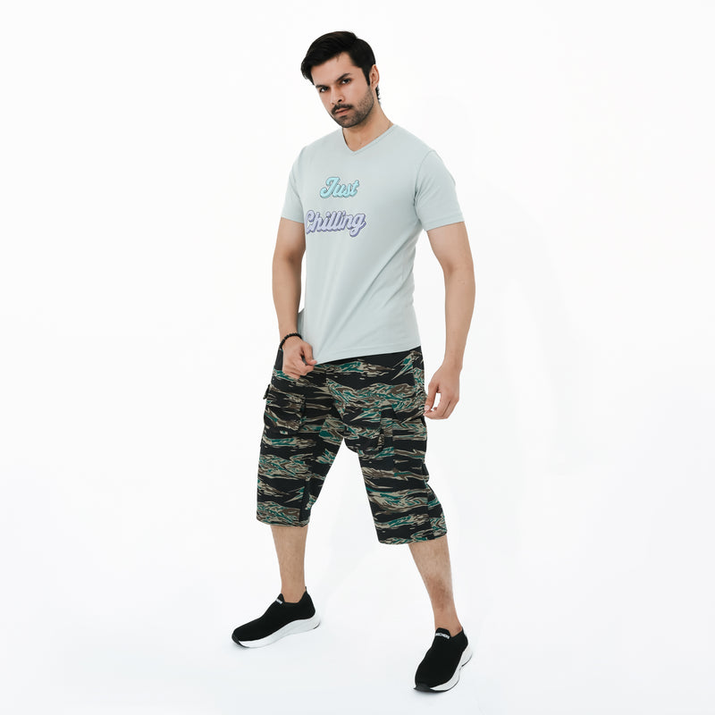 Man wearing a light gray t-shirt with text and camouflage shorts on a white background