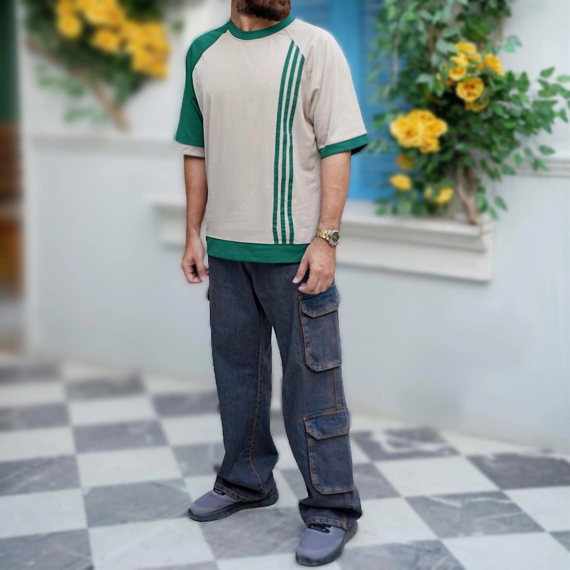 Person wearing a beige and green shirt with blue jeans standing on a checkered floor.