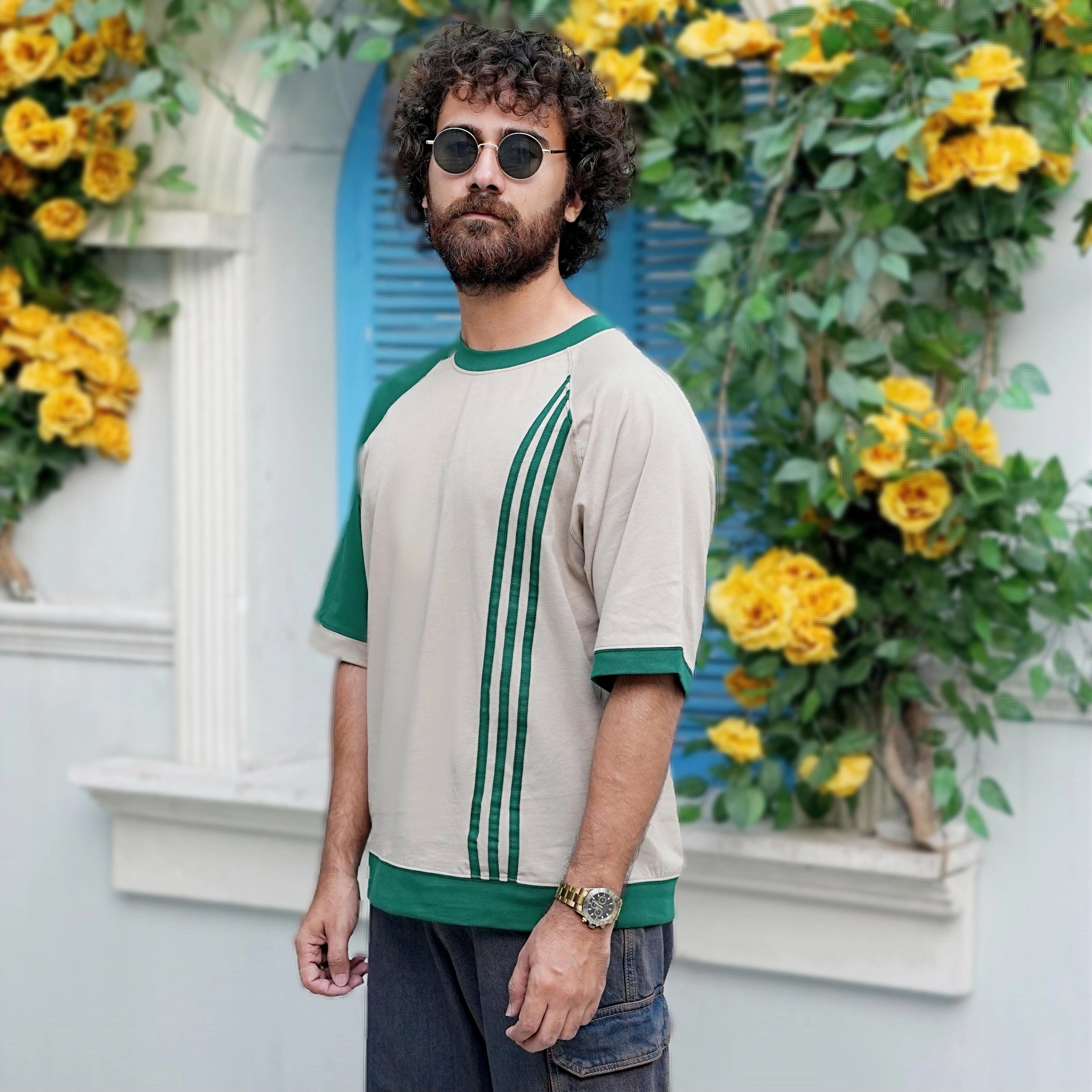 Man wearing a beige and green shirt with floral decorations in the background