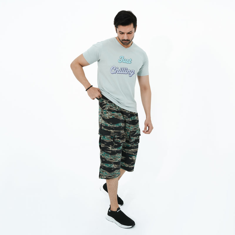 Man wearing a light gray t-shirt with text and camouflage shorts on a white background