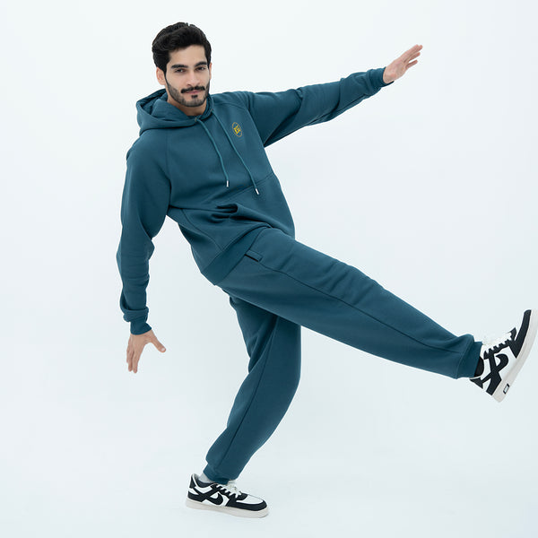 Man wearing a green tracksuit with black and white sneakers on a light gray background