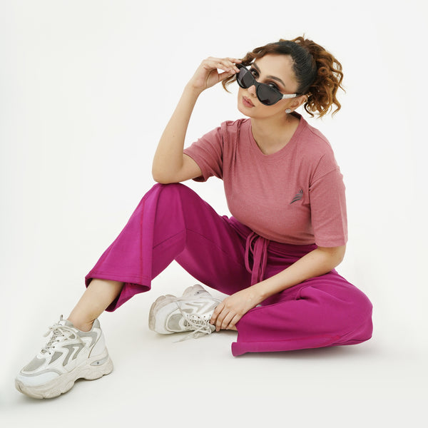 Woman wearing BSG pink shirt and magenta pants sitting on the floor with sunglasses on a white background