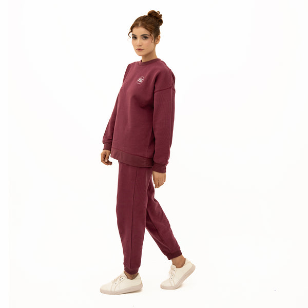 Woman wearing a maroon tracksuit with a logo on a white background