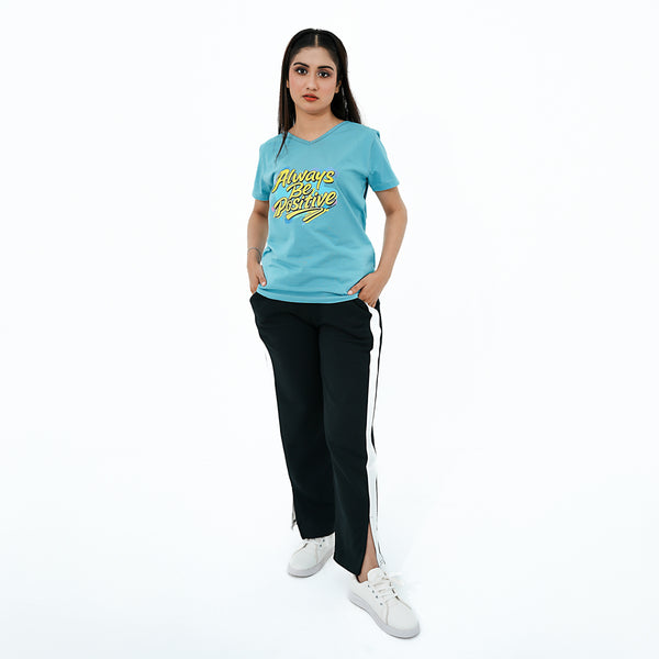 Woman wearing a blue t-shirt with yellow text and black pants with a white stripe on a white background
