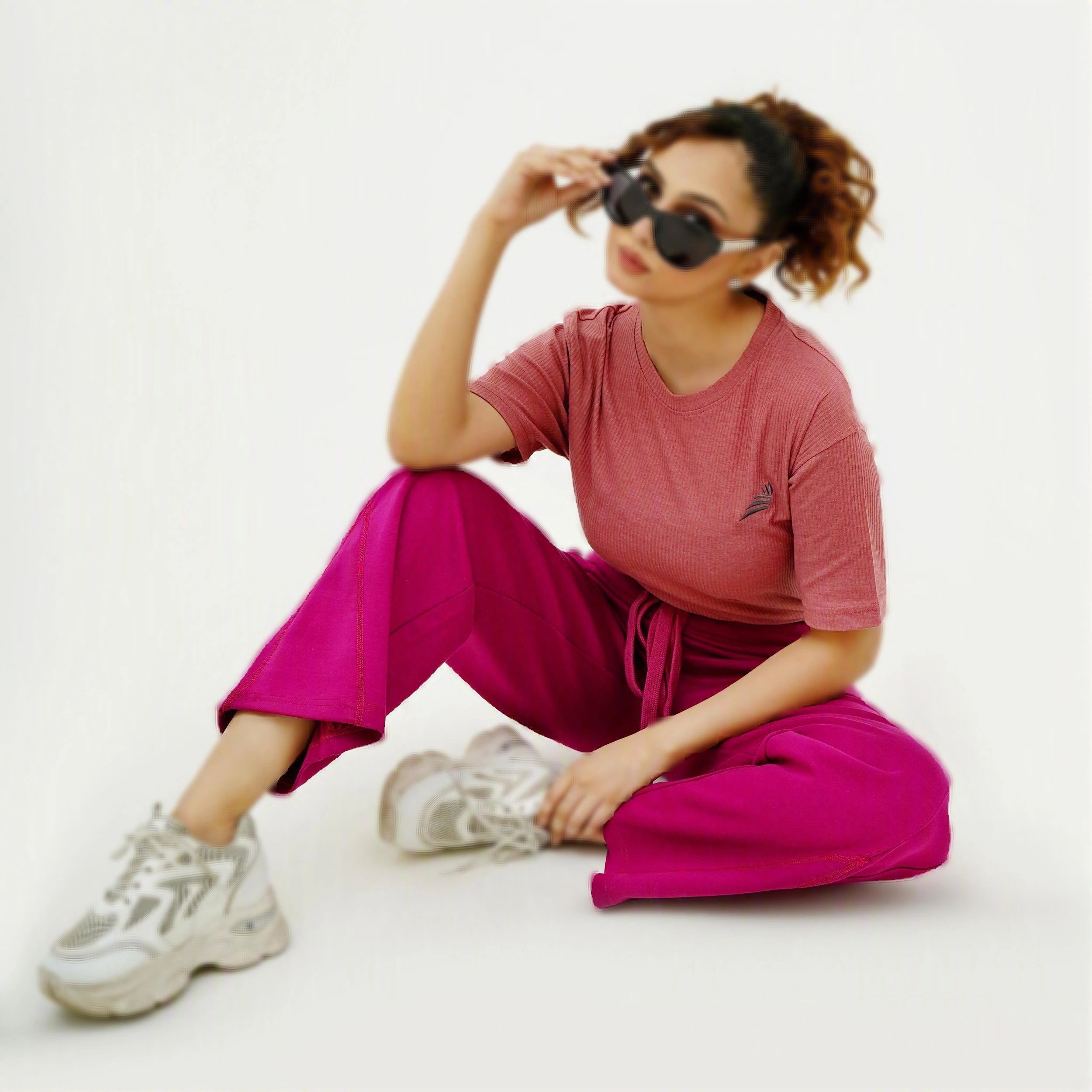 Person wearing a pink outfit with sunglasses on a white background