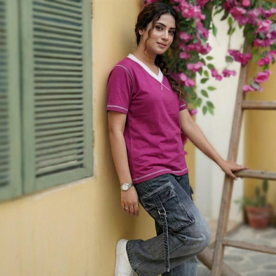 Woman in a pink shirt leaning against a yellow wall with green shutters and pink flowers.