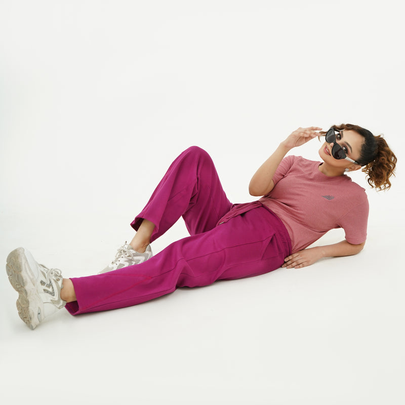 Woman wearing BSG pink top and purple pants sitting on a white background